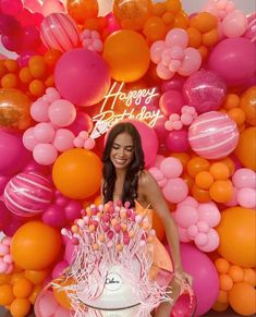 a woman standing in front of a cake with candles on it and balloons all around her