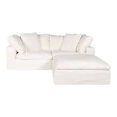 a white sectional couch with pillows on it's back and footstool in the middle