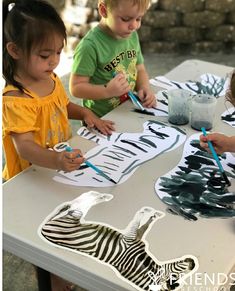 three children are sitting at a table painting zebras