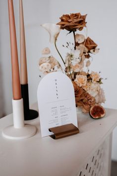 an arrangement of flowers, candles and menu cards on a white table with gold accents