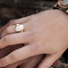 a woman's hand with a gold ring on top of her finger and a white shell in the middle