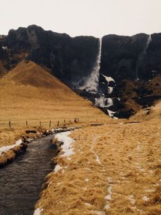 a stream running through a dry grass covered field with mountains in the background and snow on the ground