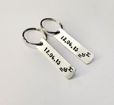 two personalized silver key chains with date and year engraved on the front, set against a plain white background