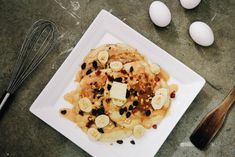 pancakes with bananas, raisins and butter on a white plate next to eggs