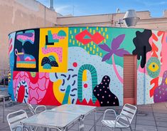 an outdoor dining area with tables and chairs painted in bright colors on the side of a building