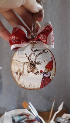 a hand holding a christmas ornament with an image of a deer on it