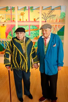 an older man and woman standing next to each other in front of colorful paintings on the wall