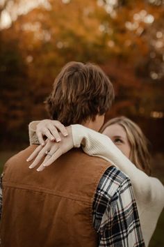 a man and woman embracing each other in front of trees