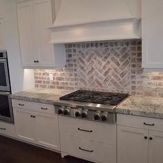 a kitchen with white cabinets and marble counter tops, an oven and stove top in the center