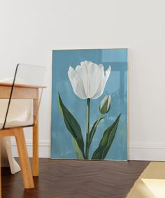 a white flower sitting on top of a wooden floor next to a table and chair