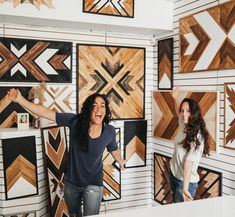 two women standing in front of wooden wall art