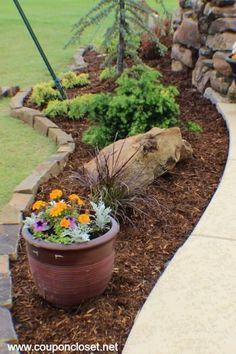 a planter filled with lots of flowers next to a stone wall and grass field