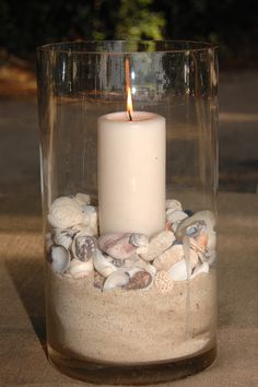 a lit candle in a glass filled with sand and shells