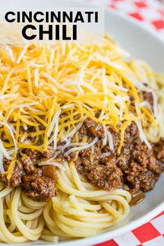 a white bowl filled with spaghetti topped with ground beef and cheese on a checkered table cloth