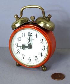 an orange alarm clock sitting next to a penny