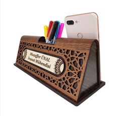 a wooden desk organizer with pens, pencils and an iphone in the back ground