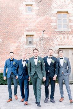 a group of men standing next to each other wearing suits and bow ties in front of a brick building