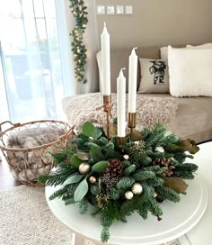 a christmas centerpiece with pine cones, greenery and candles on a coffee table