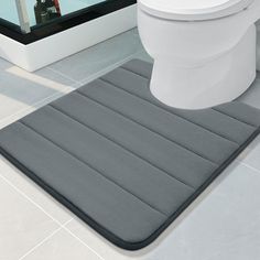 a white toilet sitting next to a gray rug on top of a tiled bathroom floor