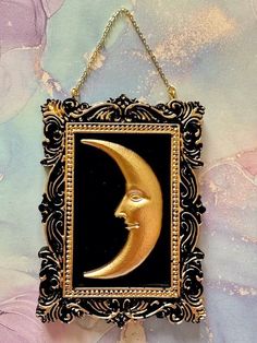 a gold and black frame with a crescent moon hanging from it's side on a wall