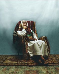 an old man sitting in a chair on top of a rug