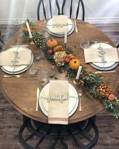 a wooden table topped with white plates covered in fall decorations and place settings on top of it