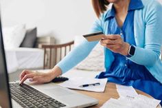 a woman sitting in front of a laptop computer holding a credit card