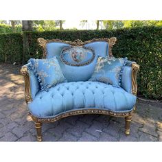 a blue couch sitting on top of a brick floor next to a hedge covered in bushes