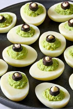 deviled eggs topped with guacamole and black olives on a pan