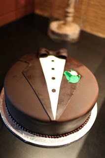 a chocolate cake decorated with a tuxedo and bow tie on a black table