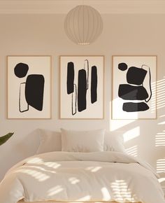 three black and white paintings hanging on the wall above a bed in a room with sunlight coming through windows