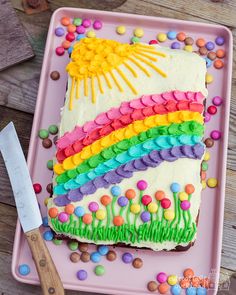 a rainbow cake on a pink plate with a knife