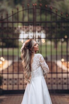 a woman standing in front of an iron gate wearing a white wedding dress with long sleeves