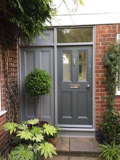 a grey front door with two potted plants on either side and brick building in the background