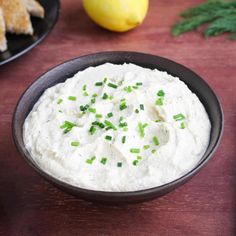 a bowl of mashed potatoes with chives and lemon wedges on the side