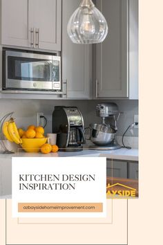 a kitchen with gray cabinets and yellow fruit on the counter top in front of a silver microwave oven