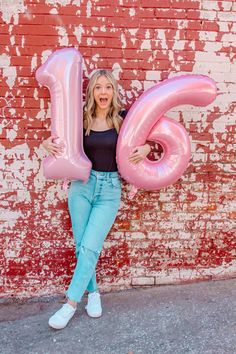 a woman holding up the number six balloon in front of a brick wall