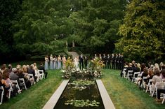 a wedding ceremony in the middle of a garden with water and flowers on the aisle