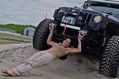 a woman laying on the ground next to a jeep with her hands in the air