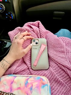 a woman is laying in the car with her phone case on her lap, and she's wearing a pink tie dye sweater