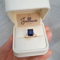 someone is holding an engagement ring with a blue stone in it's gift box