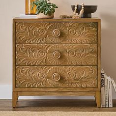 an ornate wooden chest of drawers with books on the bottom and two plants sitting on top