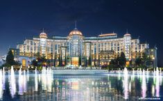 the hotel is lit up at night with water fountains in front and lights reflecting on the ground