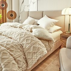 a bed with white comforter and pillows in a bedroom next to a chair, lamp and window