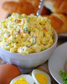 an egg salad in a white bowl next to some croissants