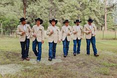 a group of men in cowboy hats standing next to each other on top of a grass covered field