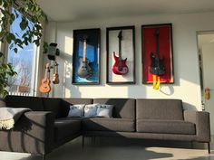 three guitars are hanging on the wall above a couch in front of a large window