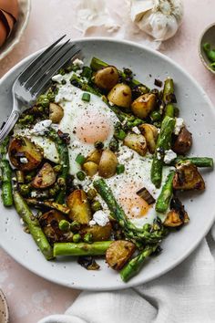 a white plate topped with asparagus, potatoes and an egg on top of it