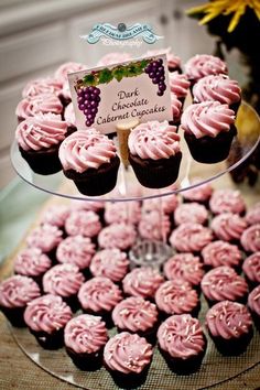 cupcakes are displayed on a glass platter with a sign that says dark chocolate and pink icing