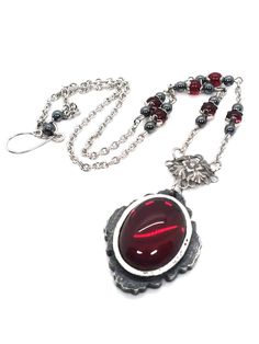 Made to Order! Made for stalking the crumbling halls of haunted castles, this amulet is a vampire lover's treasure. A wonderful accessory for your gothic wardrobe that calls to mind a stately vampire languishing on their rotting estate, eagerly awaiting visitors. With this gothic talisman, you're sure to be invited in! The cabochon is set in a hand cast pewter bezel and accompanied by matching handmade stainless steel chain links. The remainder of the dainty chain is stainless steel as well. Cur Gothic Garnet Jewelry For Gift, Handmade Gothic Necklaces For Larp, Adjustable Black Vampire Style Necklaces, Vampire Pendant, Red Gothic Chain Necklace, Red Gothic Necklace, Collectible Gothic Metal Necklace, Vampire Necklace Pendants, Gothic Collectible Pendant Necklace